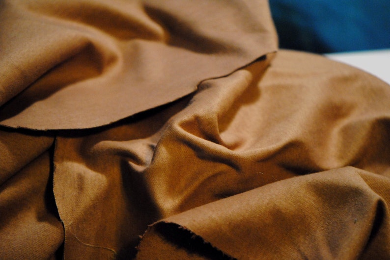 May include: A close-up of a brown fabric with a soft, textured surface. The fabric is folded and draped, creating a sense of depth and dimension.