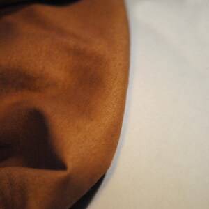 May include: Close-up of a brown fabric with a soft, textured surface. The fabric is folded and draped, creating a smooth, flowing curve.