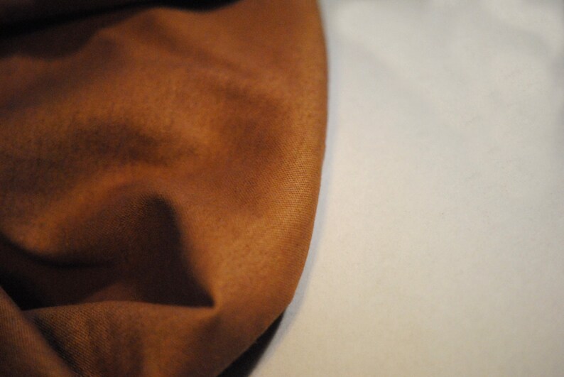 May include: Close-up of a brown fabric with a soft, textured surface. The fabric is folded and draped, creating a smooth, flowing curve.