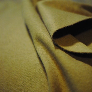 May include: A close-up of a folded piece of fabric. The fabric is a muted olive green color and has a soft, textured surface.