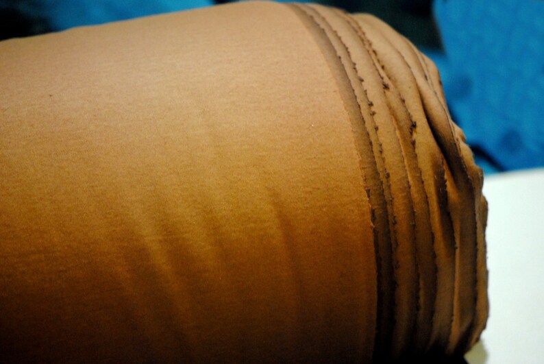 May include: A close-up of a brown fabric roll with a textured surface. The fabric is rolled up tightly and has a dark brown seam running along the edge.