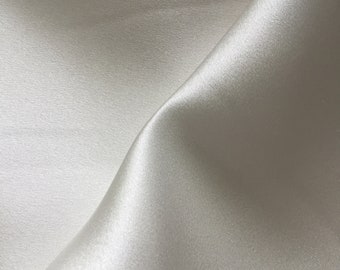 May include: A close-up of a smooth, white satin fabric with a subtle sheen. The fabric is folded in a way that creates a soft, flowing curve.