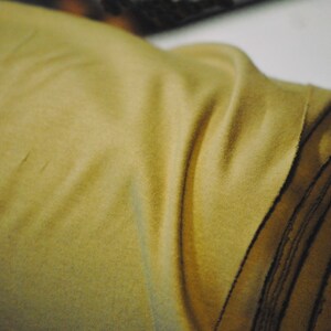 May include: A close-up of a large roll of fabric. The fabric is a light brown color and has a soft, fuzzy texture.