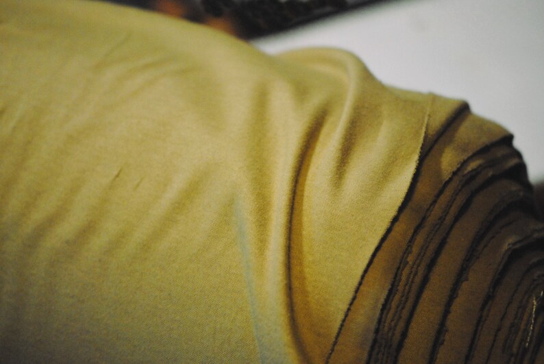 May include: A close-up of a large roll of fabric. The fabric is a light brown color and has a soft, fuzzy texture.