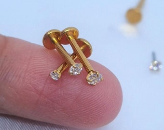 May include: Three gold body jewelry pieces with clear rhinestones. The jewelry is on a finger.