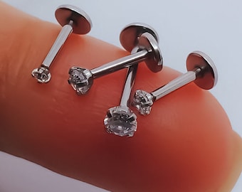May include: Four silver lip rings with clear rhinestones. The rings are arranged on a finger.