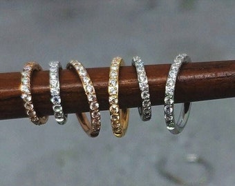 May include: Six different styles of diamond-encrusted rings, each with a different metal finish, displayed on a wooden surface.