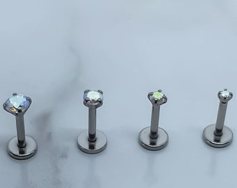 May include: Four silver body jewelry pieces with small, clear, iridescent gemstones. The jewelry is designed for lip or ear piercings.