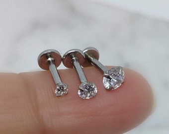 May include: Three silver barbell earrings with clear cubic zirconia stones. The earrings are different sizes.