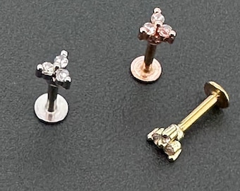 May include: Three different styles of nose rings with small clear stones set in a triangle shape. The nose rings are made of gold, silver, and rose gold.
