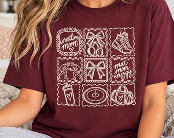 May include: A maroon t-shirt featuring a white graphic grid of nine squares. The squares contain illustrations of wrestling shoes, bows, a water bottle, a wrestling mat, a duffel bag, two wrestlers, and the text wrestling mom and mat mom energy.