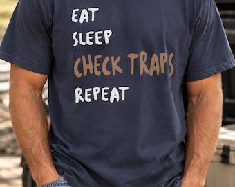 Camiseta "Comer, dormir, revisar trampas, repetir", humor sobre pesca.
