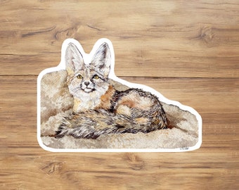 May include: A watercolor painting of a kit fox lying down on a rock. The fox has a white face with black markings around its eyes and a gray and brown body.