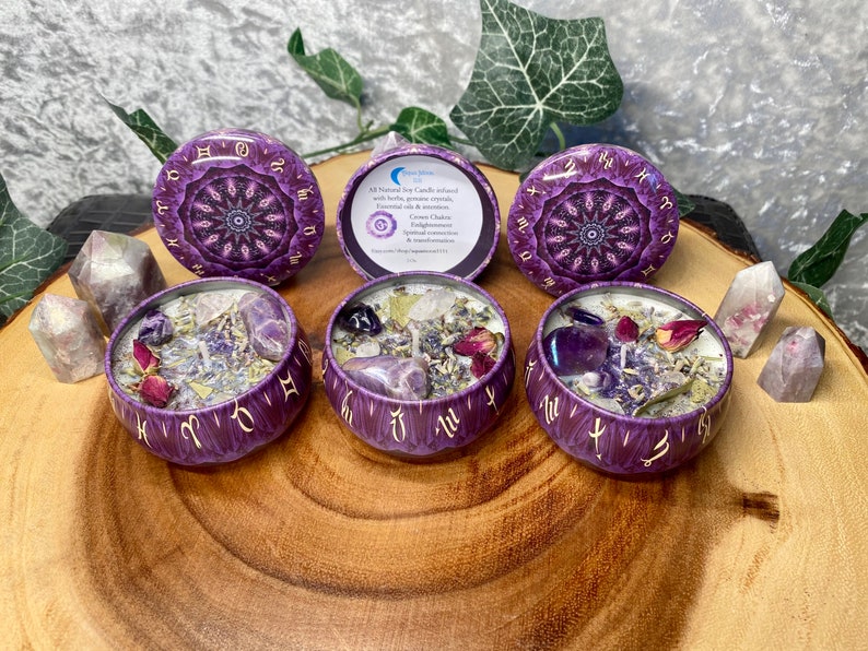 May include: Four purple and gold zodiac candles with amethyst crystals and dried flowers inside. The candles are in small round tins with a mandala design. The text on the label reads "All Natural Soy Candle infused with herbs, oils & gemstones.  Each candle is a powerful tool for spiritual connection, enlightenment & manifestation."