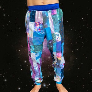 May include: Patchwork pants in shades of blue, purple, and silver. The pants feature a mix of patterned fabrics, including iridescent and textured materials. The waistband and cuffs are a solid blue color. The pants have a relaxed fit.