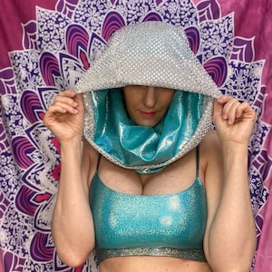 May include: A turquoise and silver hooded top with a sparkly finish. The top is worn over a turquoise sparkly crop top and a leopard print skirt.