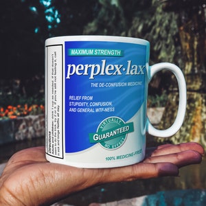 May include: White ceramic mug with a blue and white label that reads "MAXIMUM STRENGTH perplex-lax THE DE-CONFUSION MEDICINE RELIEF FROM STUPIDITY, CONFUSION, AND GENERAL WTF-NESS VIRTUALLY GUARANTEED NO EFFECT 100% MEDICINE-FREE"
