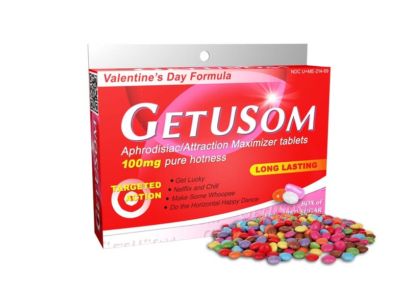 Op de afbeelding: Een rode en witte doos met de tekst "Valentine's Day Formula" en "GETUSOM Aphrodisiac/Attraction Maximizer tablets 100mg pure hotness LONG LASTING" erop. De doos heeft ook een rode cirkel met het woord "TARGETED ACTION" erin. Er liggen kleurrijke, snoep-achtige tabletten verspreid voor de doos.