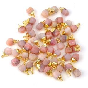 Op de afbeelding: Een groep roze opaal edelsteen kralen met vergulde springringen. De kralen zijn onregelmatig van vorm en hebben een natuurlijke, ruwe uitstraling.