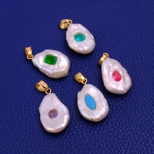 May include: Five irregularly shaped, white pearl pendants with gold-colored bails. Each pendant features a different colored gemstone: green, red, blue, purple, and green. The pendants are displayed on a blue surface.