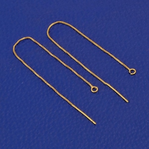 May include: A pair of gold-colored threader earrings. Each earring features a delicate chain that forms a loop, with a straight post at one end and a small loop at the other. The earrings are displayed against a blue background.