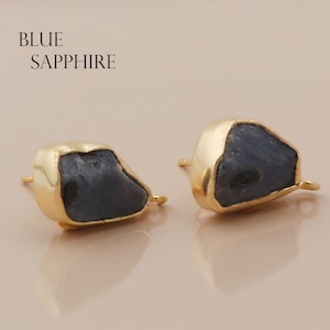 May include: A pair of gold-toned earrings with blue sapphire stones. The stones are irregularly shaped and have a rough, natural look. The earrings are a simple and elegant design.