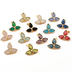 Peut inclure: Une collection de boucles d'oreilles à clous dorées, chacune avec un design à trois pétales et des accents de pierres précieuses colorées. Les pierres précieuses varient en couleur, notamment le vert, le rose, le bleu et le noir, sur fond blanc.
