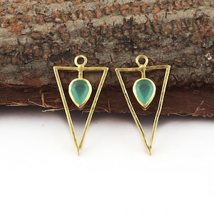 Puede incluir: Dos colgantes de metal dorado, cada uno con un marco triangular abierto y una pequeña piedra preciosa de color verde claro en forma de lágrima suspendida en el centro. Cada colgante incluye una pequeña anilla circular en la parte superior.