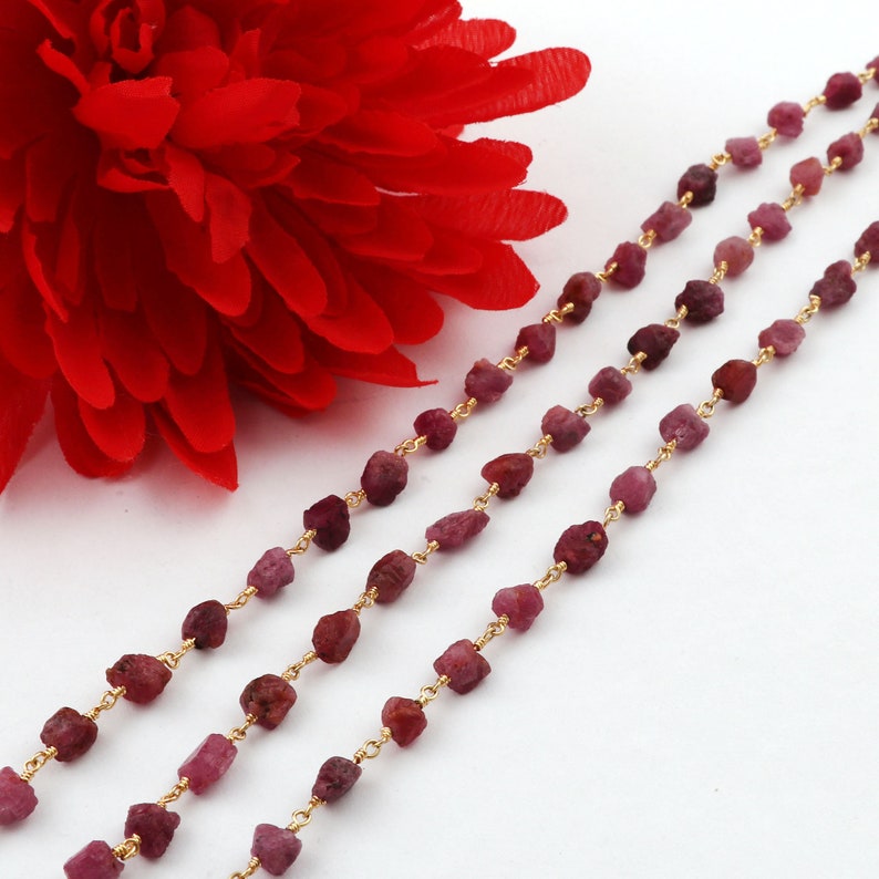 May include: Three strands of a gold chain with ruby beads. The beads are irregularly shaped and have a deep red color.