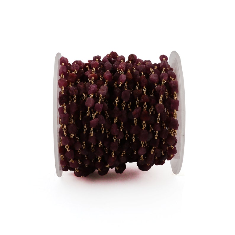 May include: A spool of ruby red gemstone beads strung on a gold chain. The beads are faceted and have a rough, natural look.