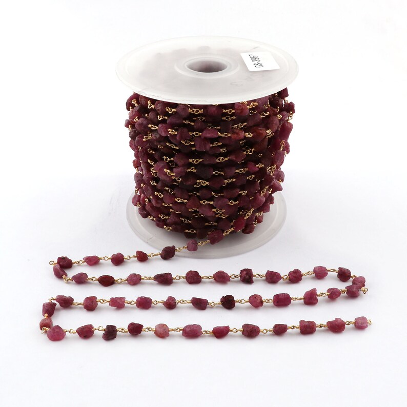 May include: A spool of ruby red gemstone beads strung on a gold chain. The beads are irregular in shape and size, and the chain is a delicate, fine link chain.
