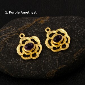 May include: Two gold-tone flower-shaped pendants with a purple amethyst gemstone in the center of each.  The pendants have a delicate, intricate design.