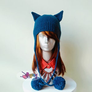 Puede incluir: Sombrero de punto azul turquesa con orejas de gato y pompones. El sombrero tiene lazos largos que se pueden atar debajo de la barbilla.