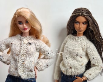 May include: Two dolls wearing long-sleeved knit sweaters in a cream-colored yarn with multicolored flecks. The doll on the left wears a button-down cardigan, while the doll on the right wears a pullover sweater. Both dolls are wearing dark blue denim jeans.