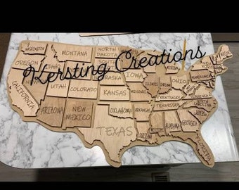 May include: A wooden map of the United States with each state outlined and labeled. The map is unfinished and has a natural wood color. The text "Kersting Creations" is written across the top of the map.