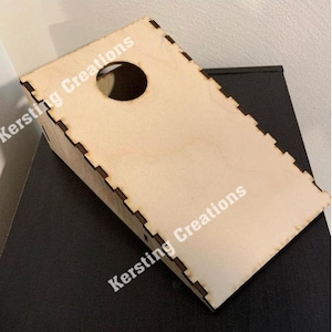 May include: A wooden, light brown, angled board with a circular hole cut out. The board has a scalloped edge and the text "Kersting Creations" is printed on the board.