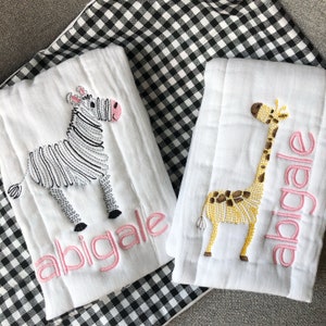 May include: Two white burp cloths with embroidered animal designs and the name "Abigale" in pink. One cloth features a zebra and the other a giraffe.