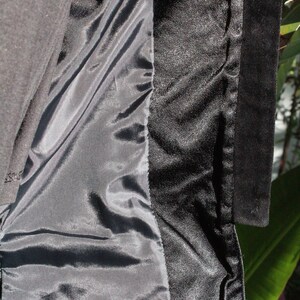 May include: Close-up of a black garment's interior, revealing a satin lining and a textured, possibly velvet, trim. The fabric is dark, with subtle variations in sheen and texture.