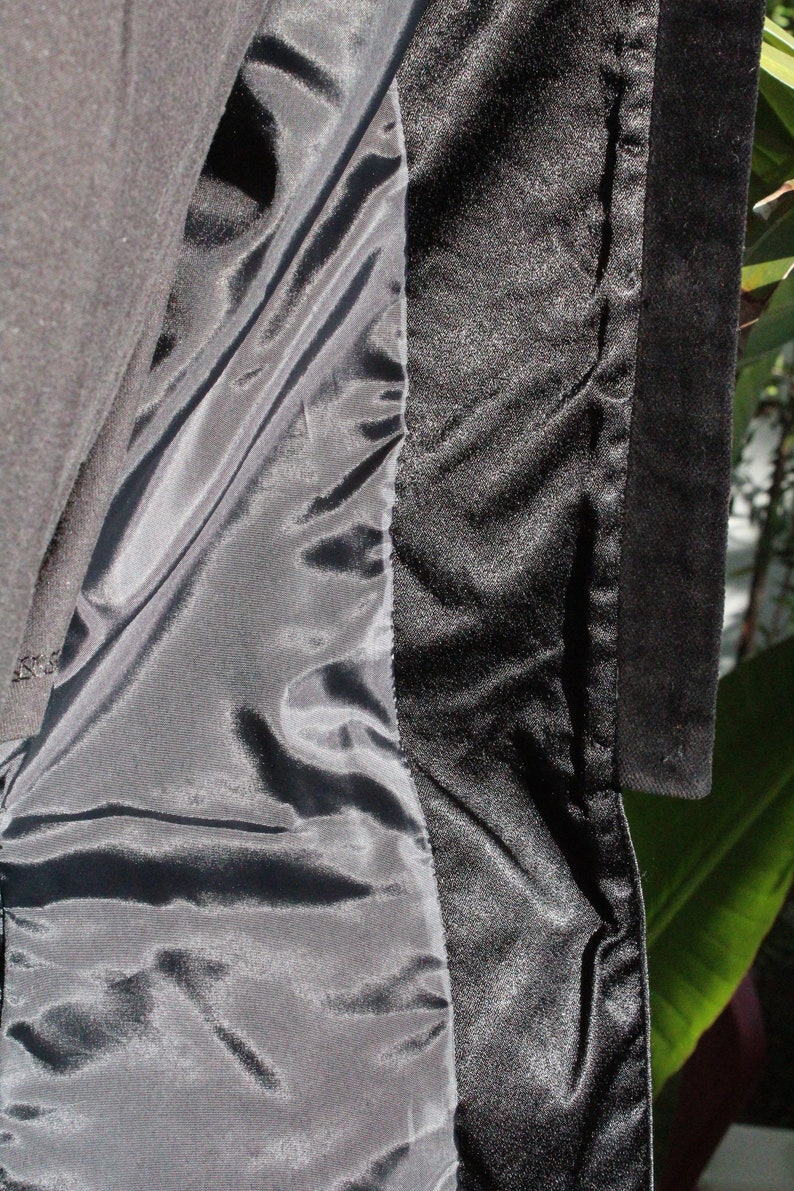 May include: Close-up of a black garment's interior, revealing a satin lining and a textured, possibly velvet, trim. The fabric is dark, with subtle variations in sheen and texture.