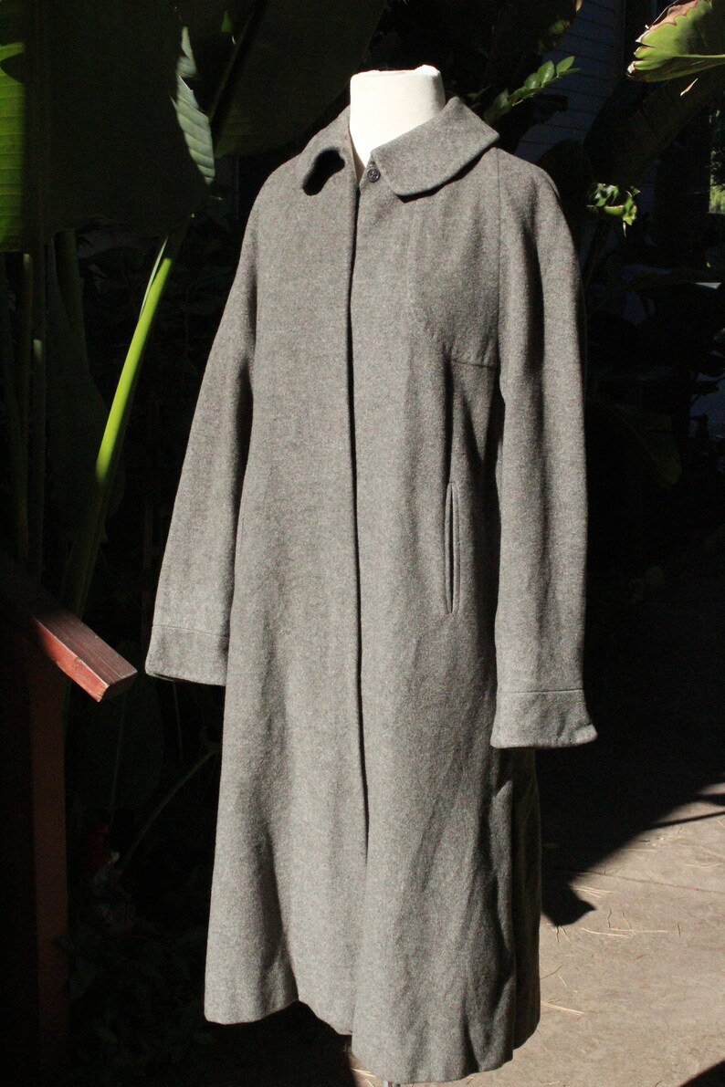 May include: A gray wool coat with a classic design. The coat features a notched collar, a single-button closure, and a tailored fit. It has long sleeves with cuffs and a front pocket. The coat is displayed on a mannequin.