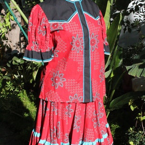 May include: A red two-piece outfit with a paisley pattern, black accents, and turquoise trim. The top has short sleeves and a black collar. The skirt has a ruffled hem. The outfit is displayed on a mannequin.