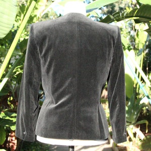 May include: A dark gray velvet blazer with a tailored fit, featuring a classic collar and buttoned cuffs. The jacket is displayed on a mannequin, showcasing its structured silhouette and elegant design. The blazer is a versatile piece for various occasions.
