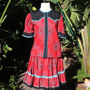 May include: A red two-piece outfit with a floral pattern, black accents, and turquoise trim. The top has short sleeves and a round neckline. The skirt is a matching length. The outfit is displayed on a mannequin.