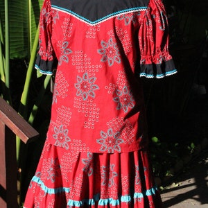 May include: A red two-piece outfit with a floral pattern and turquoise accents. The top has a black yoke and ruffled sleeves. The skirt has a tiered design with turquoise and black trim. The outfit is displayed on a mannequin.