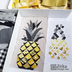 May include: A close-up of a pineapple quilt block made with black and yellow fabric scraps. The pineapple is made up of many small pieces of fabric, each with a different pattern. The quilt block is surrounded by a white background. The image also includes a pineapple coloring chart with the text "Pineapple Coloring Chart" and the text "Jitka Design Inc."