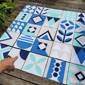 Può includere: Una trapunta realizzata con quadrati di tessuto con motivi geometrici in tonalità di blu, bianco e turchese. I quadrati sono disposti in un motivo a griglia. La trapunta è stesa su una superficie di legno. Il testo "@JITKADESIGN" è visibile nell'angolo in basso a destra dell'immagine.
