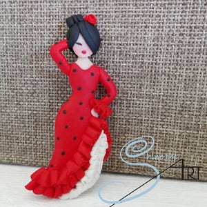 May include: A red and black polka dot dress with white ruffles. The dress is worn by a small doll with black hair and a red flower.