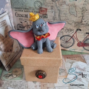 DUMBO hecho a mano en arcilla polimérica sobre cajita de cartón