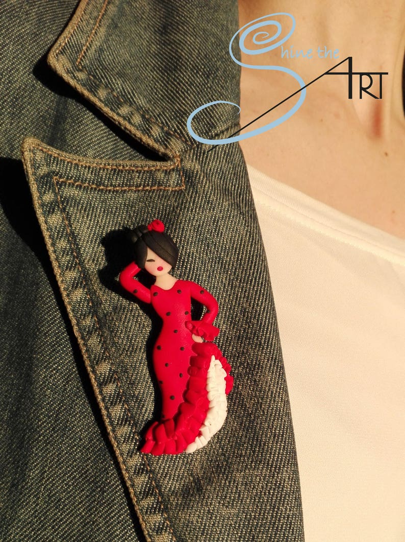 May include: A red and black polka dot flamenco dancer figurine with a white ruffled skirt. The figurine is made of polymer clay and is attached to a denim jacket.