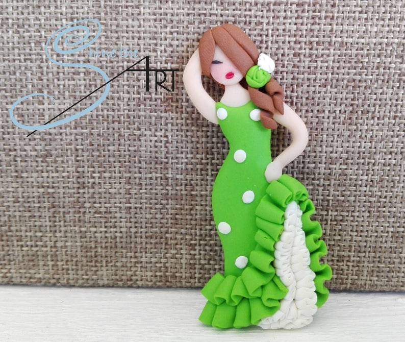 May include: A green and white polka dot dress with a white ruffle trim. The dress is made of polymer clay and is a figurine of a woman with brown hair and red lips.